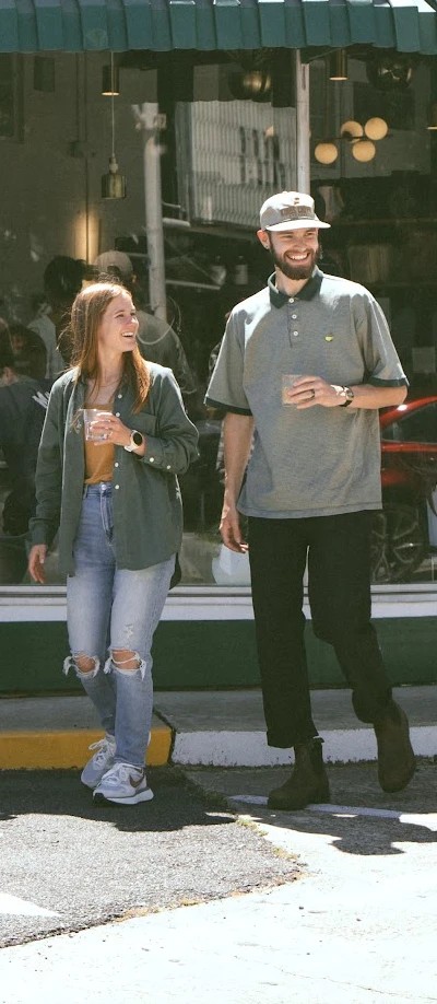 Katie and Ezra Elliott laughing as they walk out of a coffee shop with drinks in hand