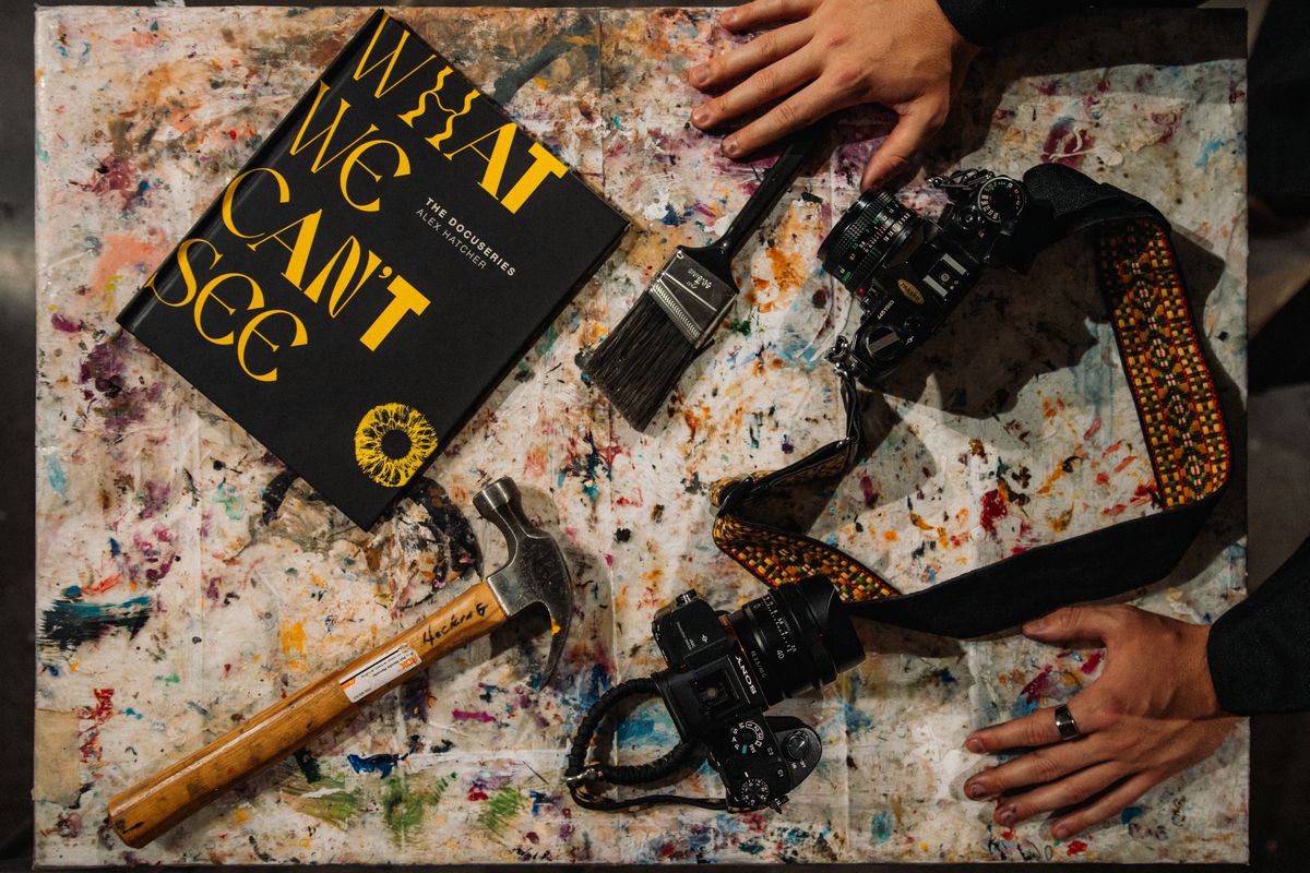 A flat lay of the book, a camera, a hammer and paint-spattered hands