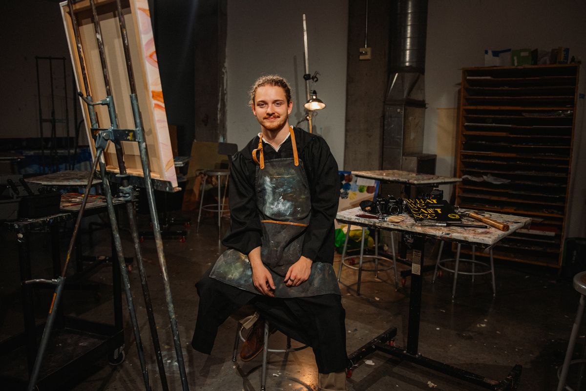 The graduate in an apron sitting among easels in an art studio