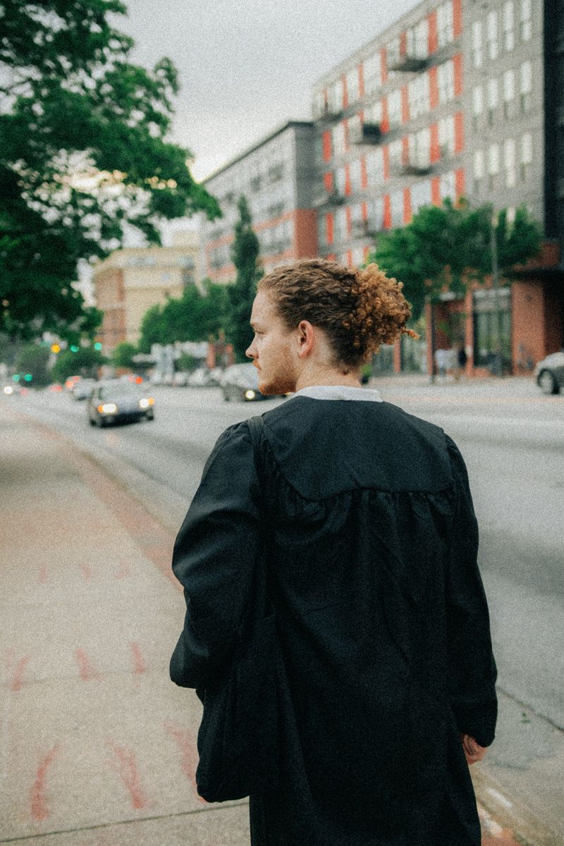 A graduate in a gown seen from behind on a city sidewalk