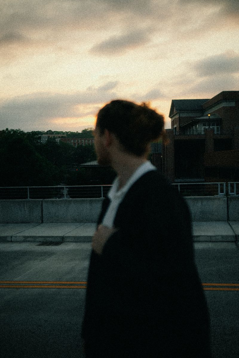 A graduate in a gown looking over his shoulder at dusk
