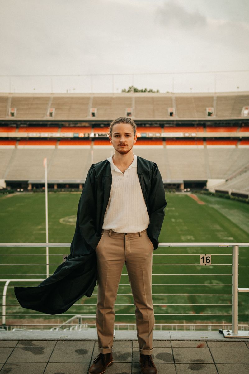 A graduate standing in an empty stadium, his gown blowing to one side