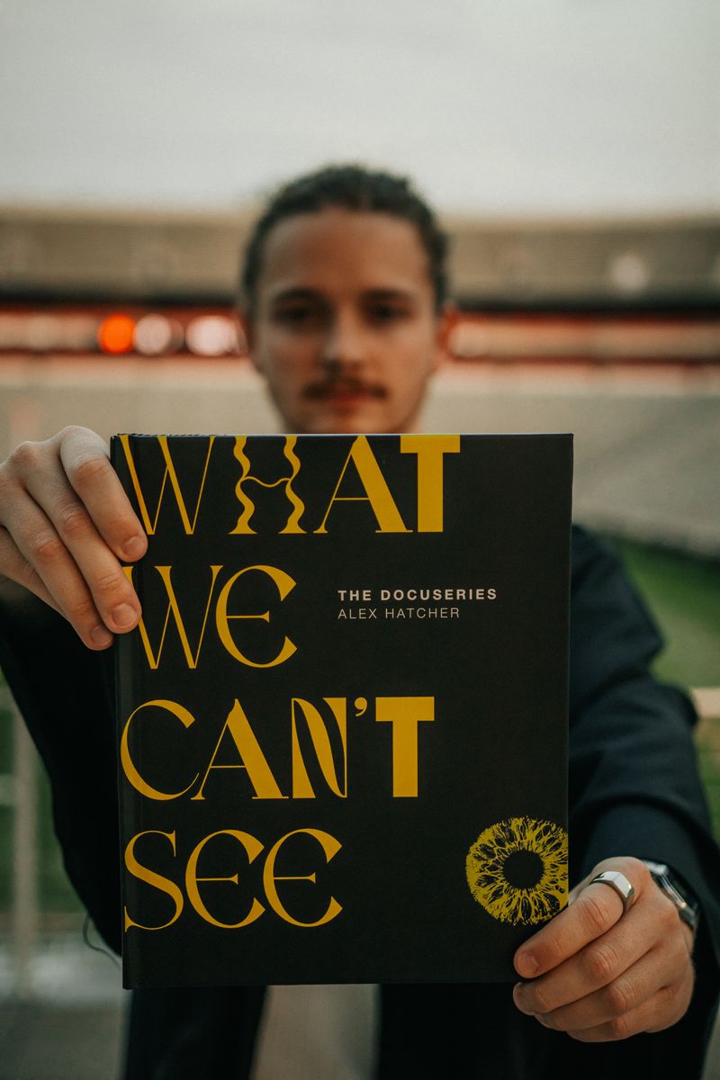 The graduate holding up a book titled What We Can't See