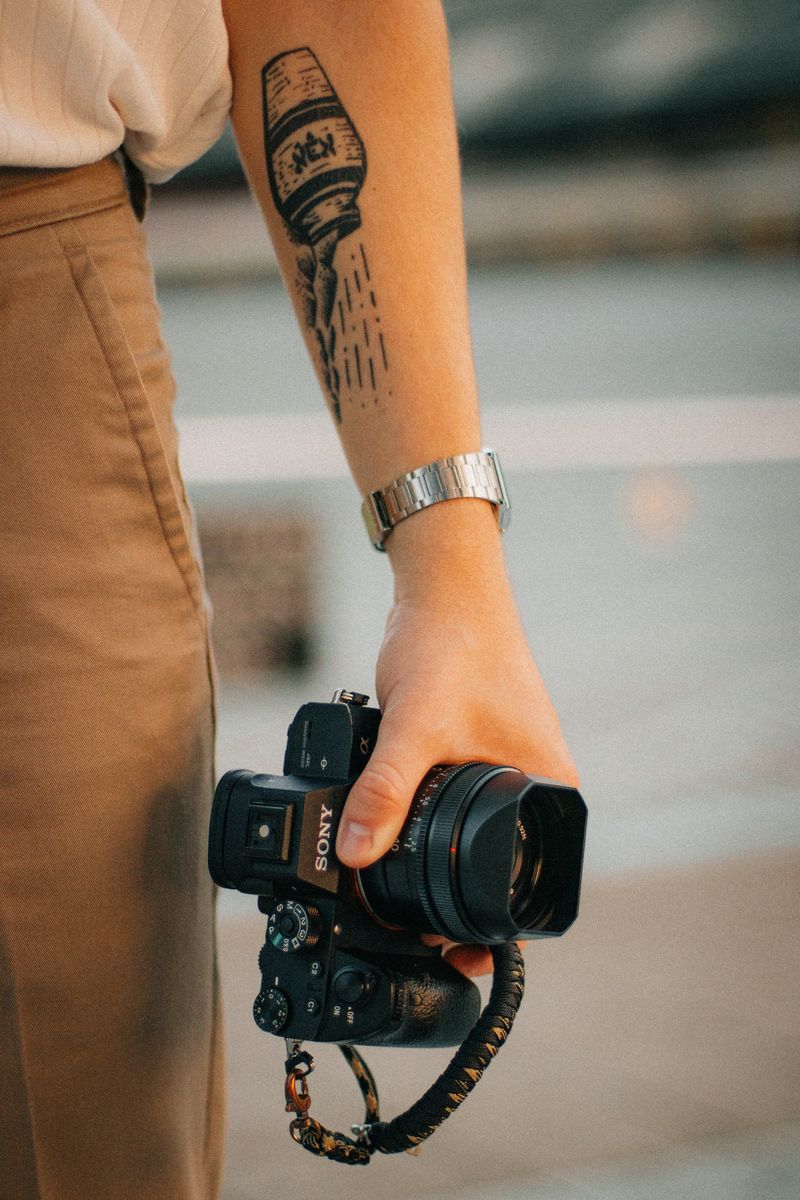A tattooed forearm holding a camera by its strap