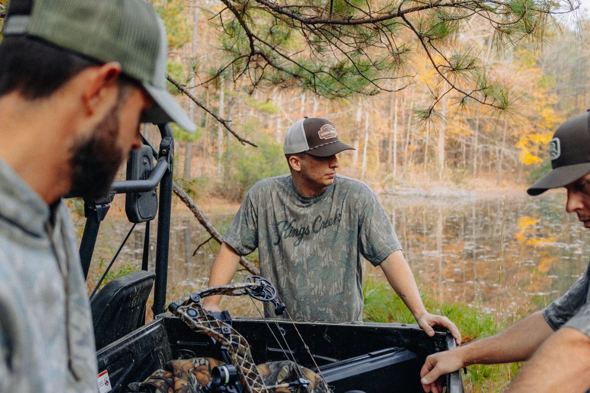 Three men gathered around a utility vehicle beside an autumn lake