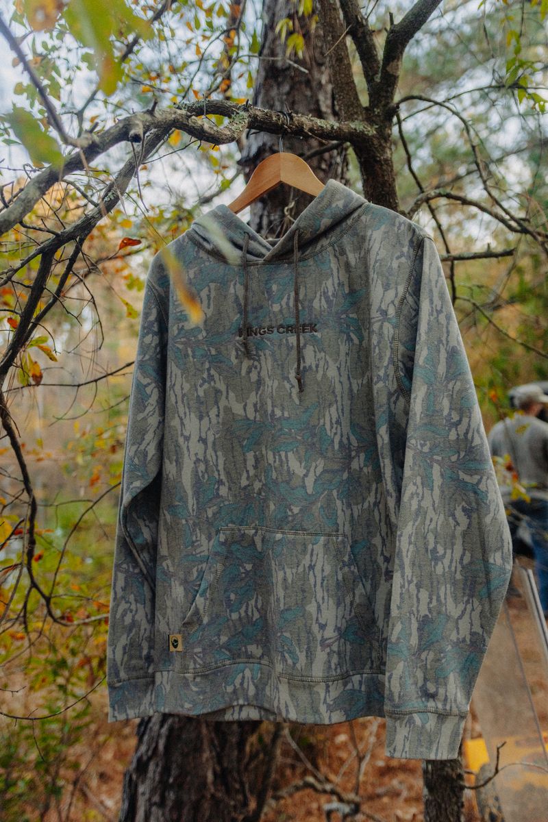 A camo hoodie on a hanger, hung from a tree branch